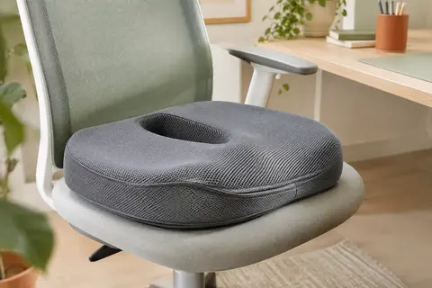 Coussin d’assise gris à ouverture centrale posé sur une chaise de bureau claire dans un espace lumineux.