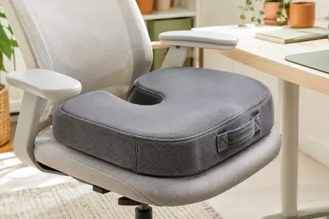 Coussin d’assise gris en forme de U posé sur une chaise de bureau, avec sa housse et sa poignée visibles.