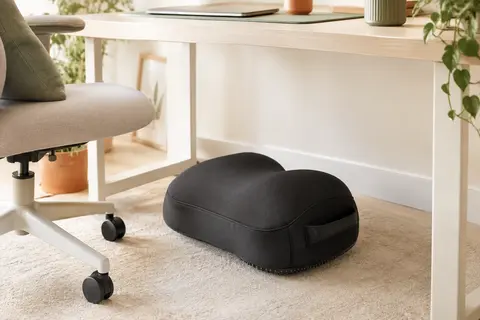 Repose-pieds rembourré noir en forme de nuage, placé sous un bureau clair dans un espace de travail lumineux.