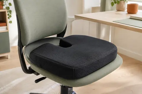 Coussin d’assise noir à découpe coccyx posé sur une chaise de bureau, avec housse en maille respirante